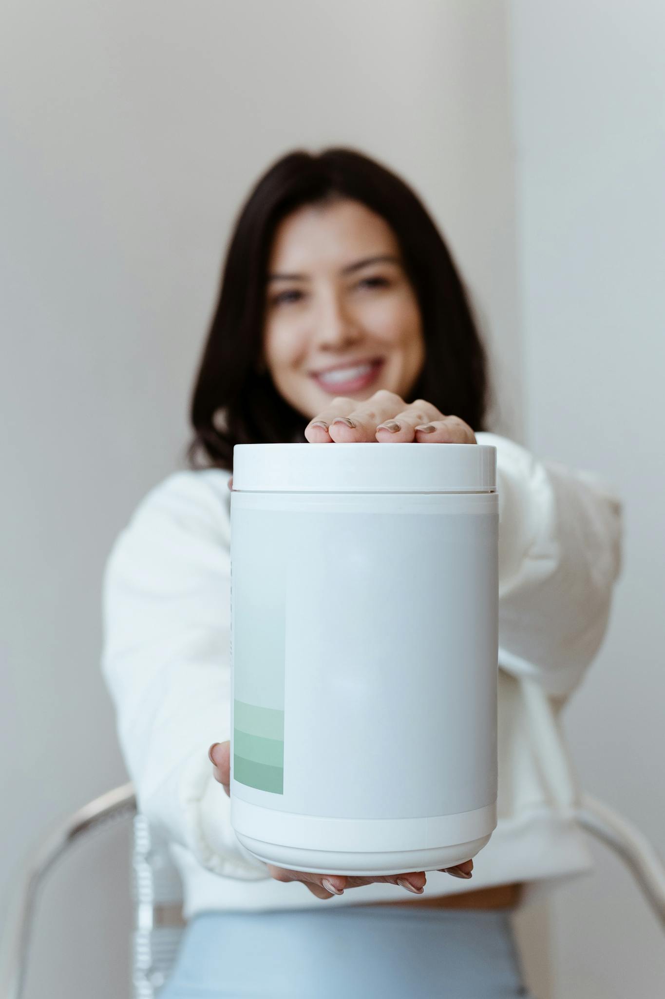 A cheerful woman presenting a container of health supplements against a minimalist background.