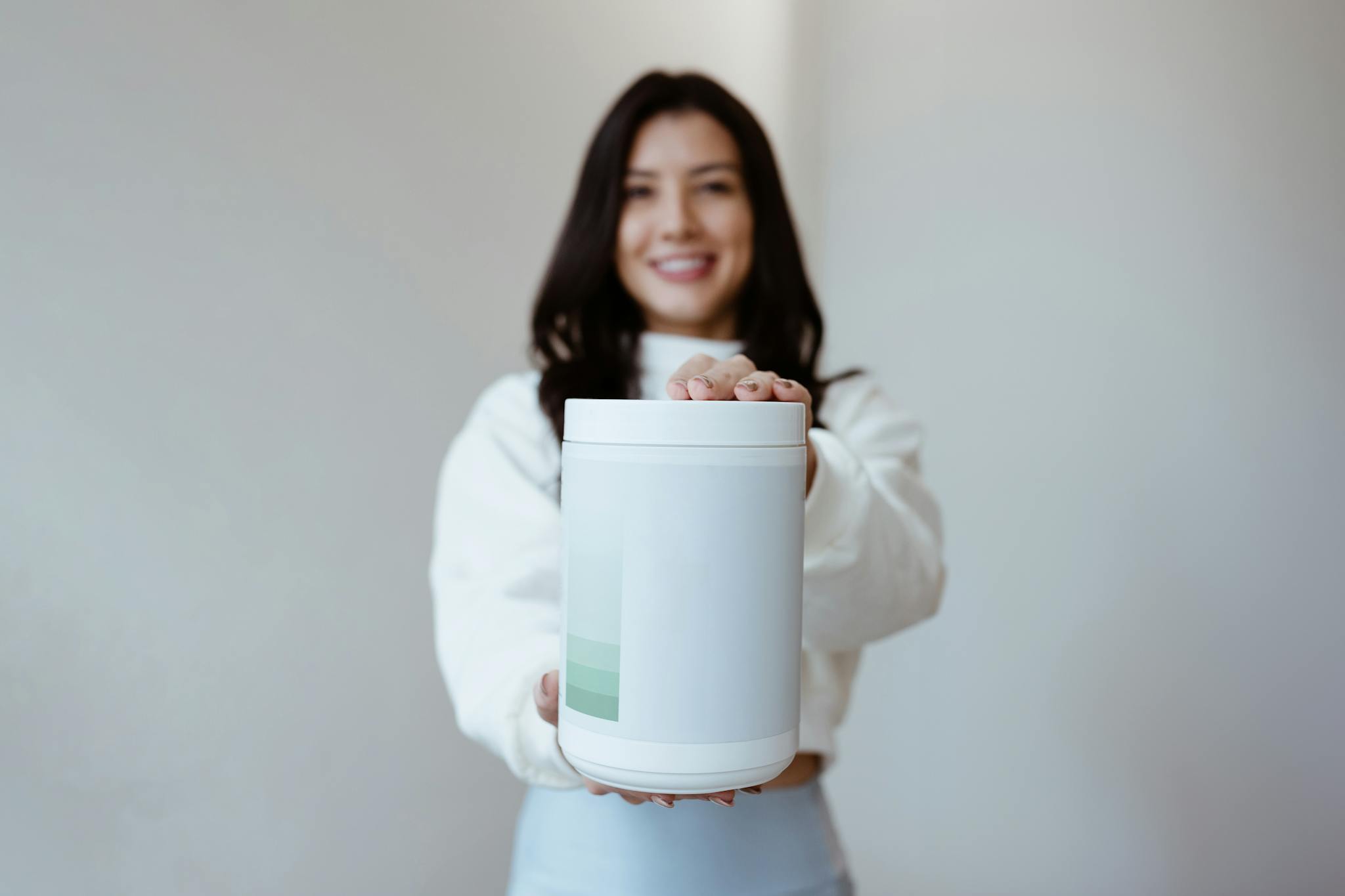 Brunette woman smiling while holding a blank container, perfect for product mockup.